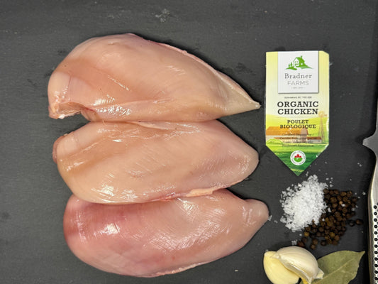 Three raw chicken breasts arranged on a dark gray surface with a small package of Birdie's Organic Chicken broth, salt, garlic, peppercorns, and bay leaves nearby.