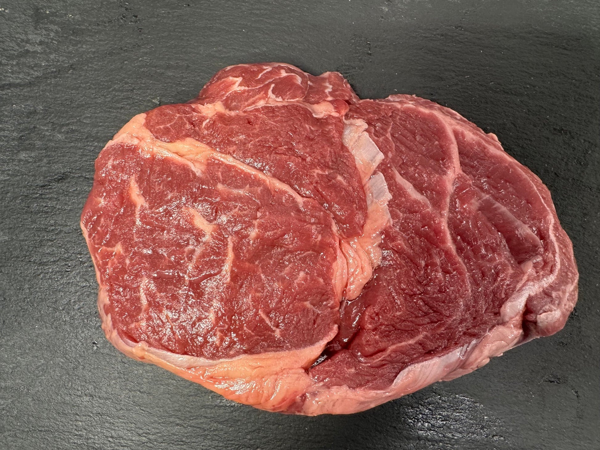 A raw beef chuck roast with visible marbling, placed on a dark textured slate surface.