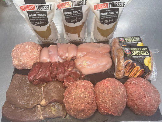 An assortment of grass fed beef and organic chicken on a slate board, with Nourish Yourself Bone Broth (beef and chicken), plus Mad Brit Chicken and Apple Sausages