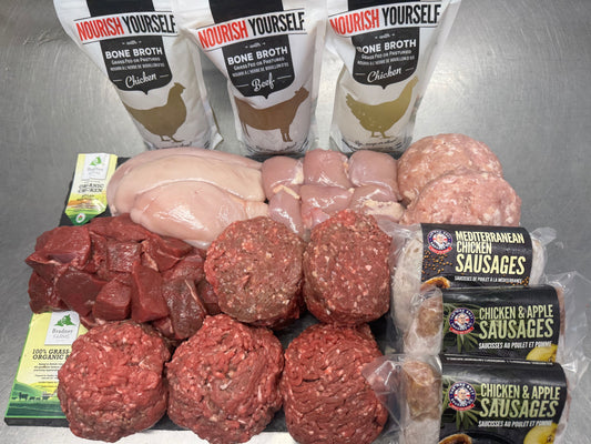 Certified organic BC family meat box contents on a steel surface: ground beef, beef stew meat, beef burgers, chicken breast, boneless skinless chicken thighs, ground chicken, Mediterranean and Chicken & Apple sausages, and 3 Nourish Yourself Bone Broth pouches