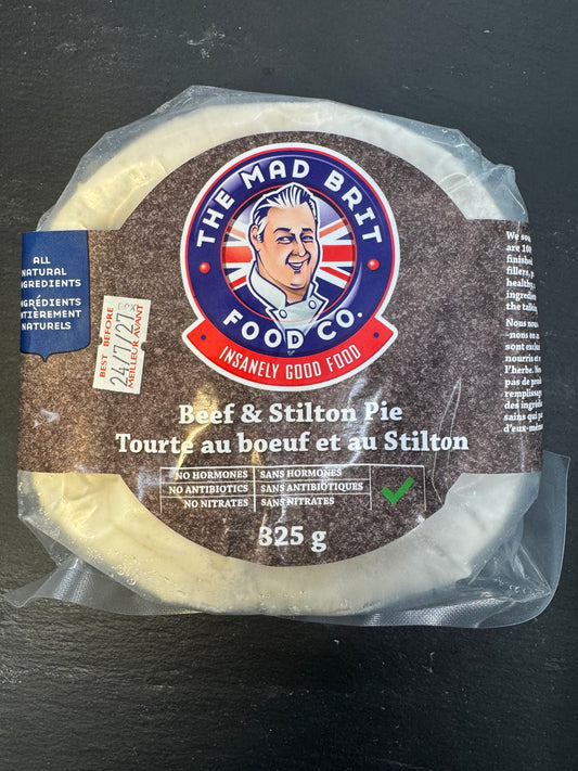 A packaged round cheese product labeled 'The Mad Brit Food Co.' and 'Beef & Stilton Pie' on a dark textured surface.